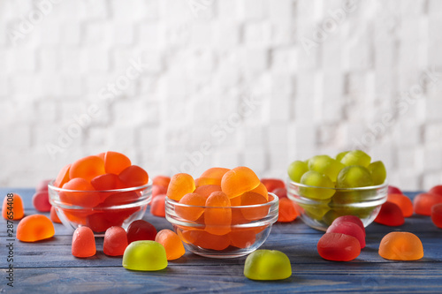 Glass bowls with tasty jelly candies on blue wooden table against white background  space for text