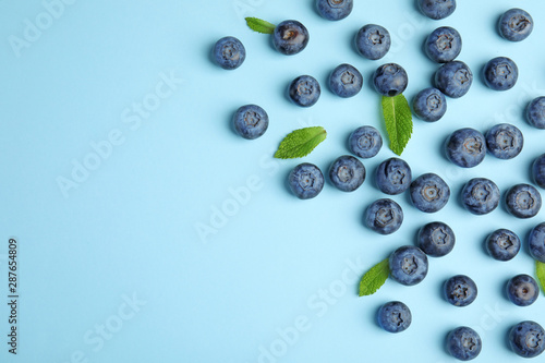 Canvas Tasty ripe blueberries and leaves on blue background, flat lay with space for te