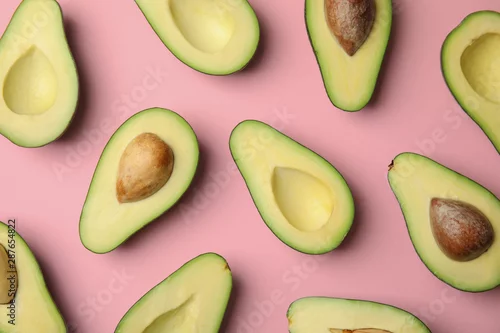 Obraz połówki awokado z pestką i bez pestki na różowym tle