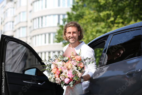 Young handsome man with beautiful flower bouquet near car on street