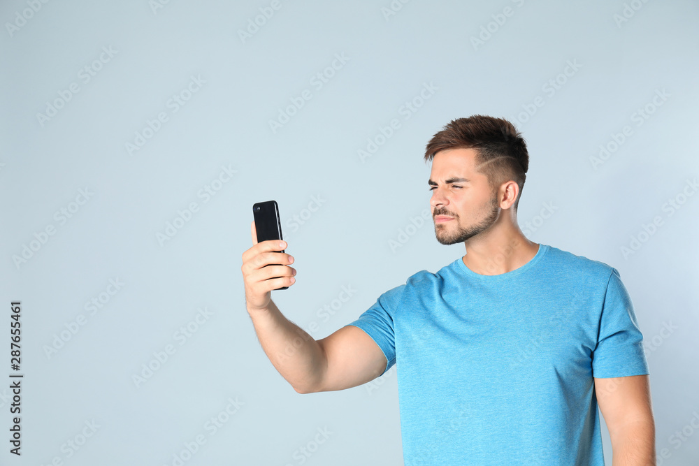 Young man with vision problems using smartphone on grey background, space for text Young man with vision problems using smartphone on grey background, space for text