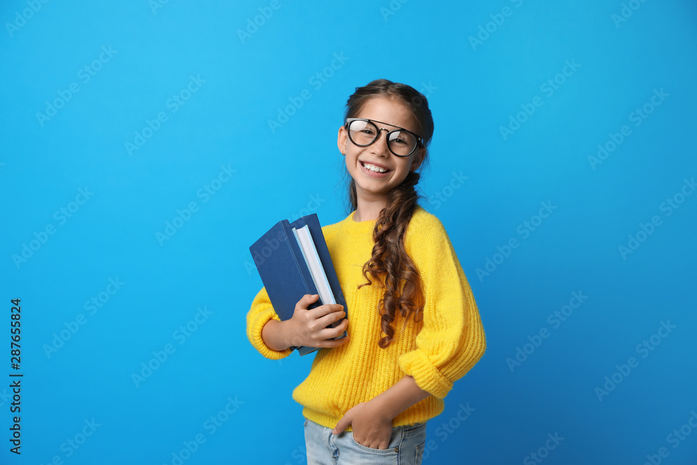 Cute little girl with glasses and books on blue background. Reading concept