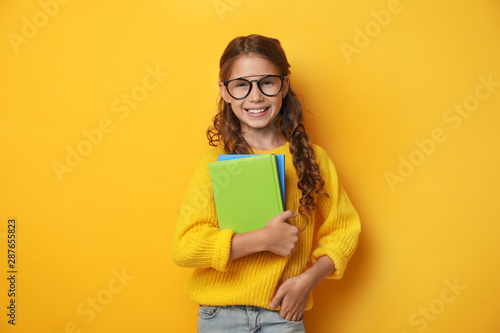 Cute little girl with glasses and books on yellow background. Reading concept