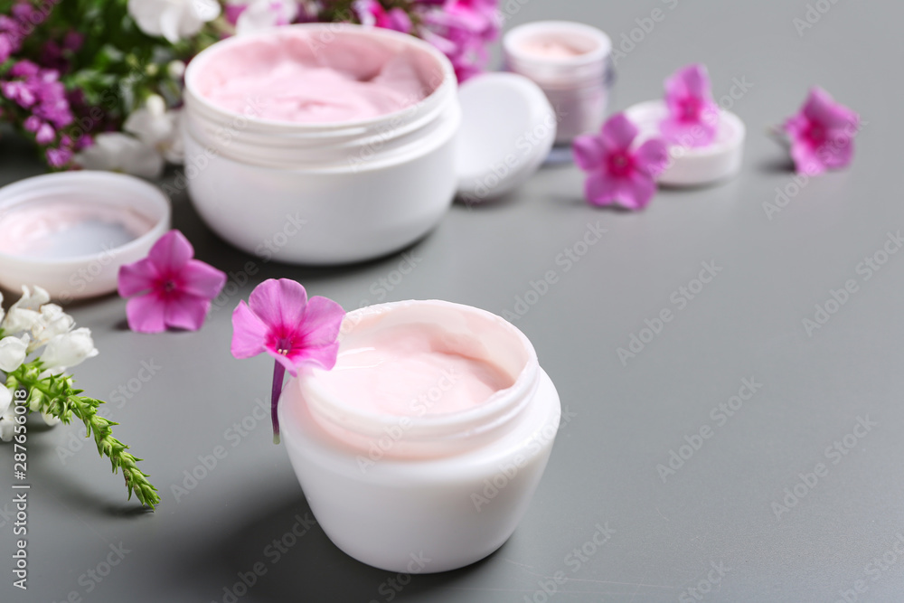 Jars of body cream and flowers on grey background Jars of body cream and flowers on grey background