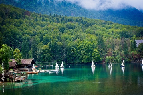 Tableau sur toile White moving boats from the port on bohinj lake in Triglav national park suround