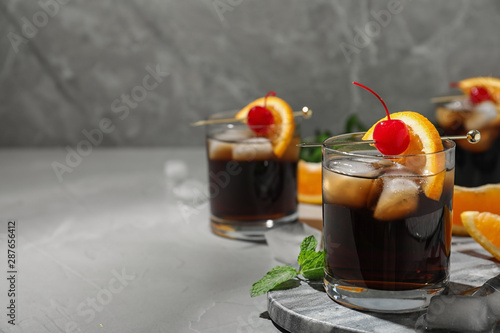 Glass of delicious cocktail decorated with cherry and orange on light grey table. Space for text