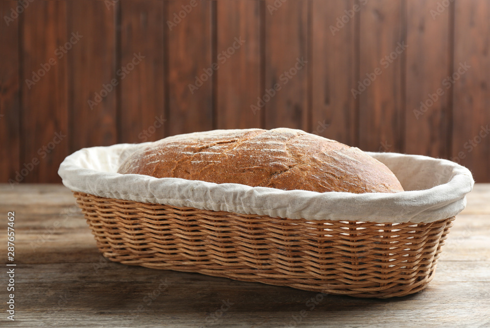 Loaf of tasty fresh bread in wicker basket on wooden table