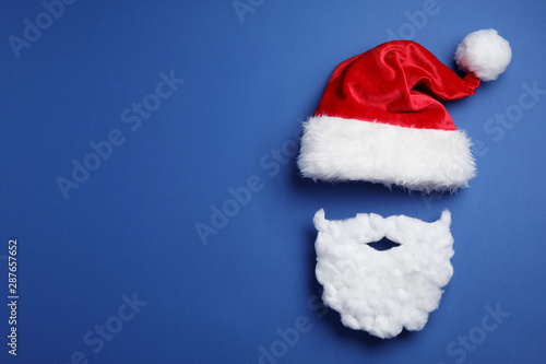Santa Claus hat and beard on blue background  flat lay. Space for text