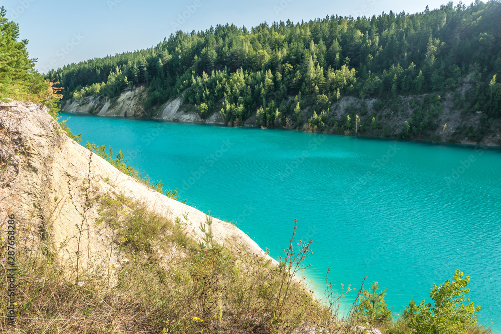 panorama of chalkpit on limestone coast of huge turquoise lake or river near forest. Chalk quarry filled with water