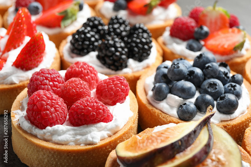 Many different berry tarts on table, closeup. Delicious pastries