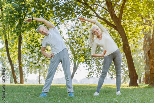 Full length of senior couple stretching together in park outdoors before yoga and fitness exercises