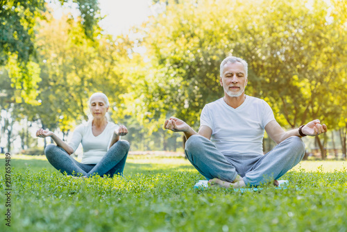 Yoga at park. Senior couple sitting in lotus pose on green grass in calm and meditation