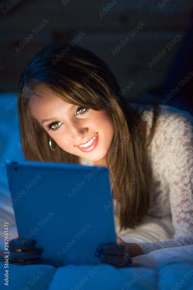 Teenage girl in the dark lying on a bed working on a tablet computer. Teenage girl in the dark lying on a bed working on a tablet computer.