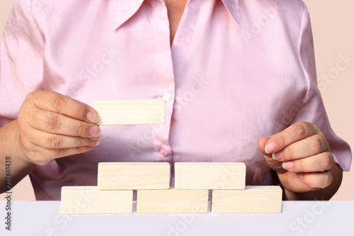 woman in a pink blouse builds a pyramid from light wooden bricks, close-up, copy space