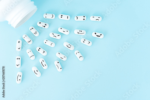  Pills with funny faces and a glass bottle on a blue background. Pharmacy antibiotic. Treating with antidepressant. Mental disorder. The concept of antidepressants and healing. Copy space. photo