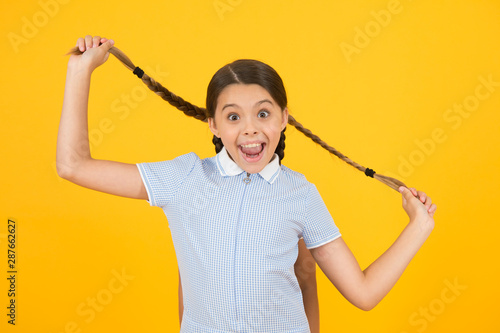 small girl in school uniform. retro look. child hold pigtail of girl behind. old school. kid fashion. happy child on yellow background. vintage fashion beauty. childhood happiness. what a surprise