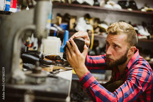Photography A handsome shoemaker with a beard repairs shoes in his workshop
