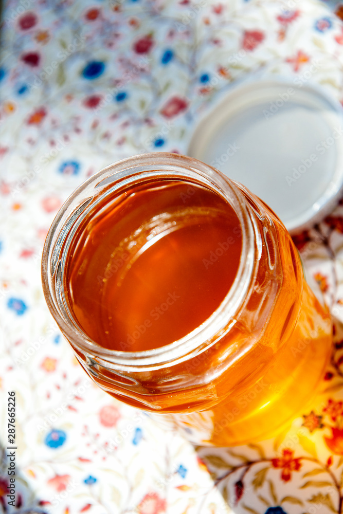 Open jar with fresh yellow organic bio honey on the colorful floral table Open jar with fresh yellow organic bio honey on the colorful floral table