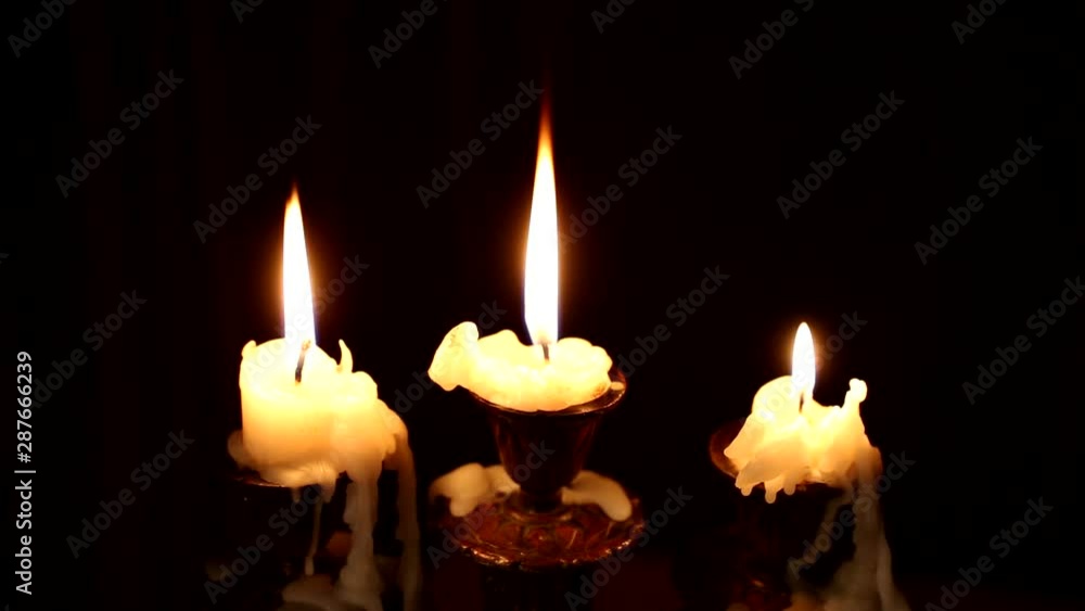 Three candles burn in a candlestick on a black background. Wind blowing