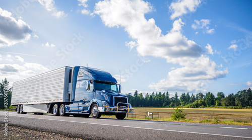 Slika na platnu Blue big rig semi truck with grille guard trabsporting frozen cargo in refrigera