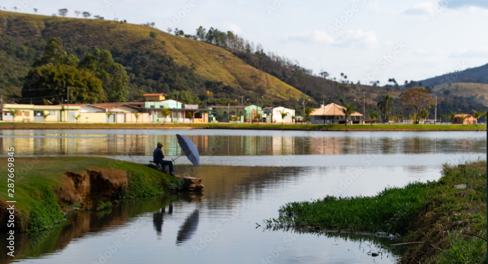 a lone fisherman shading himself from the sun with an umbrella while fishing on Capitol Lake, Minas Gerais