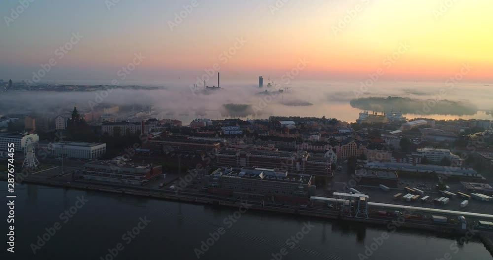 Helsinki foggy morning, Aerial, reverse, drone shot, of Katajanokka cityscape, fog clouds and colorful sky, over the baltic sea, at sunrise, on a sunny and misty autumn dawn, in Helsingfors, Finland Helsinki foggy morning, Aerial, reverse, drone shot, of Katajanokka cityscape, fog clouds and colorful sky, over the baltic sea, at sunrise, on a sunny and misty autumn dawn, in Helsingfors, Finland