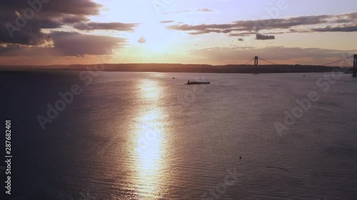 drone camera pan right over Coney Island Creek viewing a dark golden, cloudy sunset while revealing the Verrazano Bridge photo