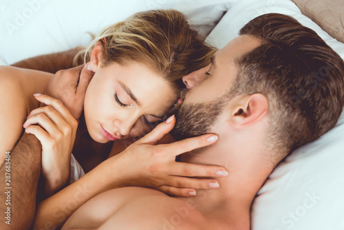 happy young couple embracing with closed eyes while lying in bed