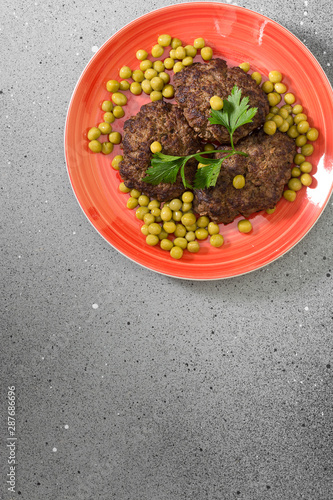 Cutlets of beef on a red plate. Grey table. Top view