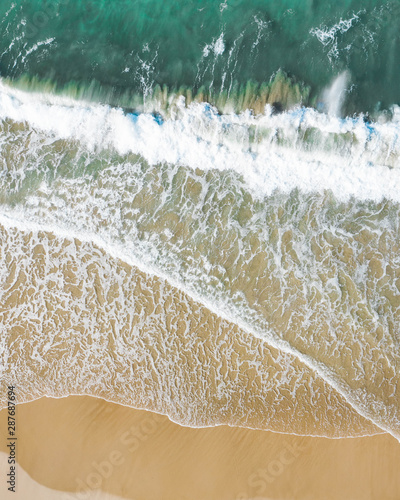 Vertical aerial of a beach at sunrise with nice white sand, blue turquoise ocean on the west coast for a holiday destination.