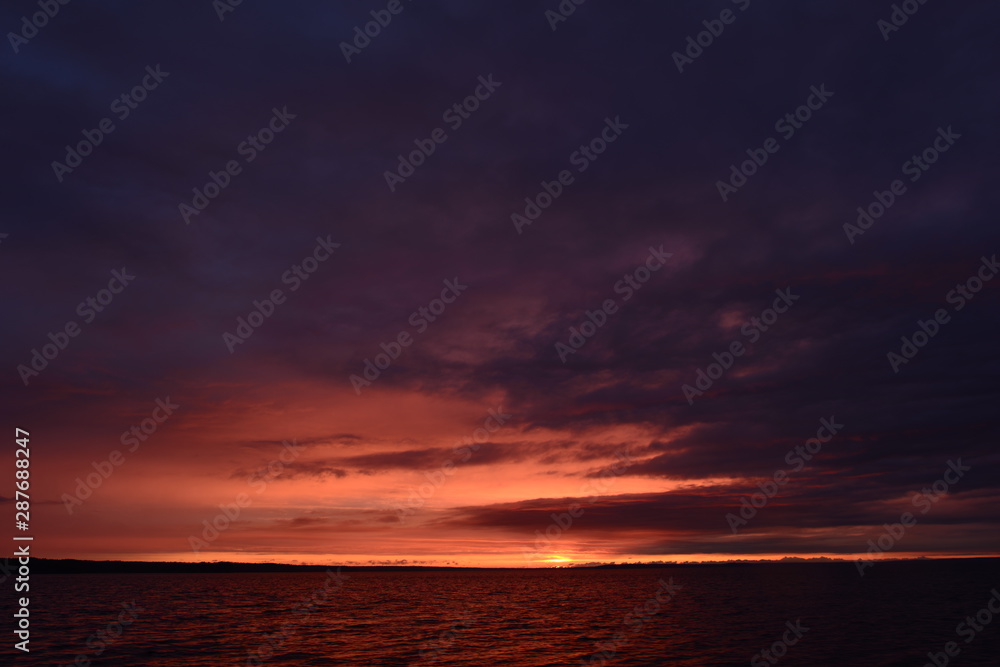 Cloudy dark blue sky in bright yellow and orange colors of sunlight at sunset