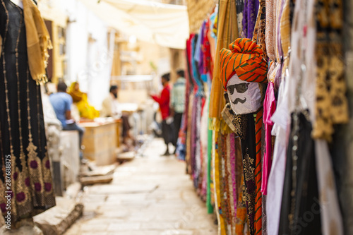 (Selective focus) Beautiful shop with colorful traditional Indian clothes (Sari) and a mask depicting a person's face from Rajasthan. Jaisalmer, India.