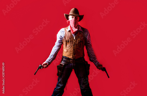 Man wearing cowboy hat, gun. West, guns. Portrait of a cowboy. owboy with weapon on red background. American bandit in mask, western man with hat. Portrait of farmer or cowboy in hat photo