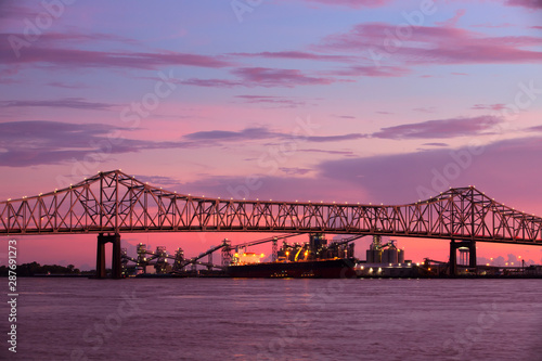 Steel bridge over Mississippi river under a stunning sunset sky in Baton-Rouge, Louisiana, with freight vessel and plant in the background