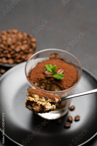 Portion of Classic tiramisu dessert in a glass cup on dark concrete background