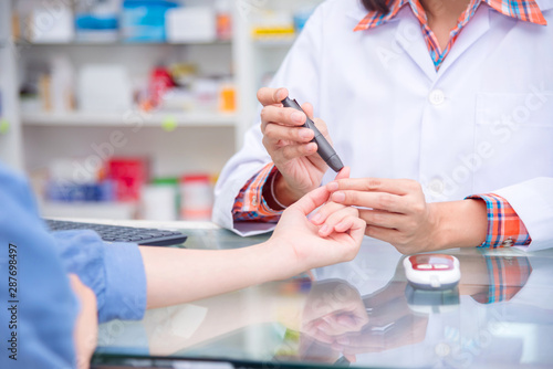 Hands of Pharmacist checking patient blood sugar by glucometer in drugstore