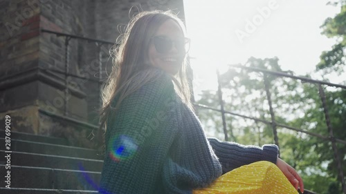 girl in sunglasses sits on stone steps in sun and she smiles, portrait photo