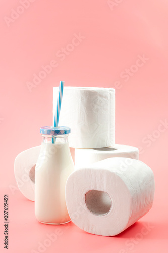 Lactose intolerance and the inability to digest milk concept theme with a bottle of milk with a blue straw and roll of toilet paper isolated on pink background photo