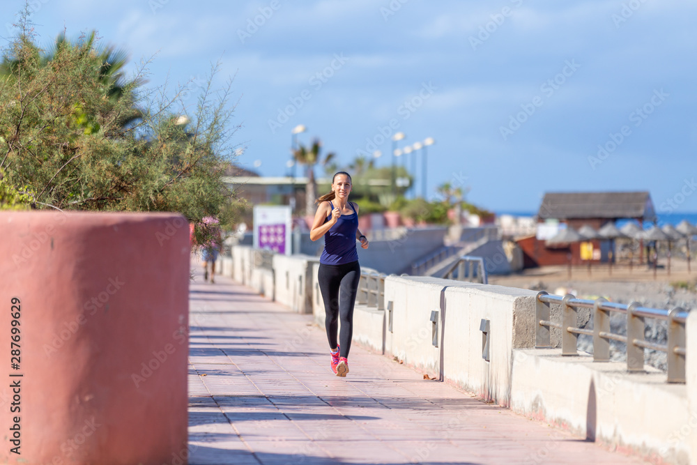 Young smiling girl jogging on the embankment in the morning