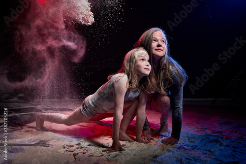 Two sisters in black studo with red and blue light during photoshoot with flour