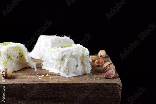 Cotton candy with pistachio on wooden board surrounded by nuts against black background photo