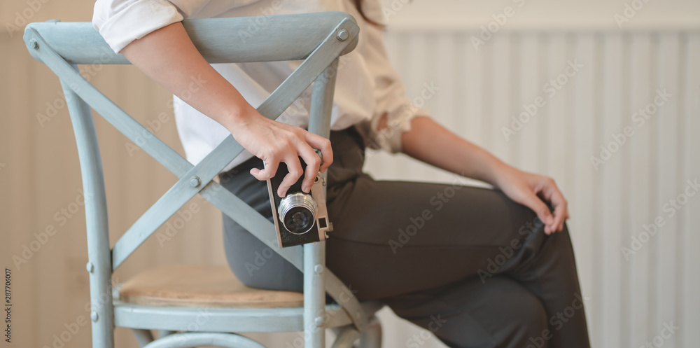 Young female photographer holding vintage camera while sitting on the chair in comfortable room