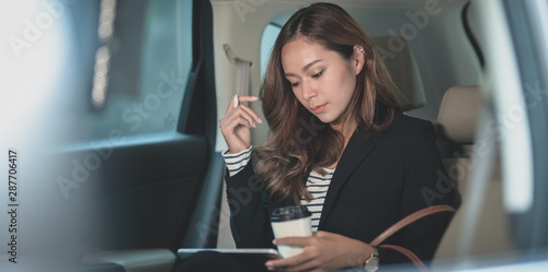 Obraz na plátně Young hard-working businesswoman working on the car with a cup of coffee