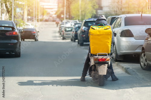 Wallpaper Mural Food delivery courier with big yellow backpack riding scooter on city street with traffic. Fast lunch takeaway delivery. Teenager job Torontodigital.ca