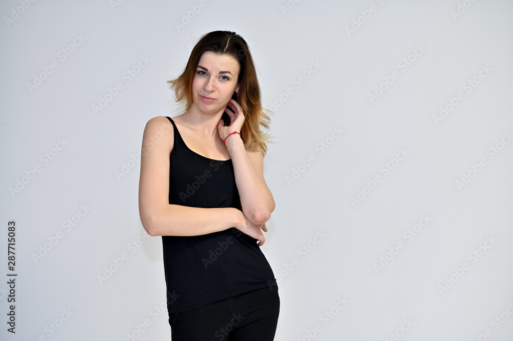 Portrait of a pretty brown-haired young woman on a white background in a black t-shirt. He stands in different poses, talking, different emotions. Portrait of a pretty brown-haired young woman on a white background in a black t-shirt. He stands in different poses, talking, different emotions.