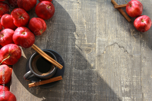 Red apples, cup of coffee and cinnamon sticks on grey wooden boards or table. Top view. Autumn, fall, morning, breakfast, healthy food concept