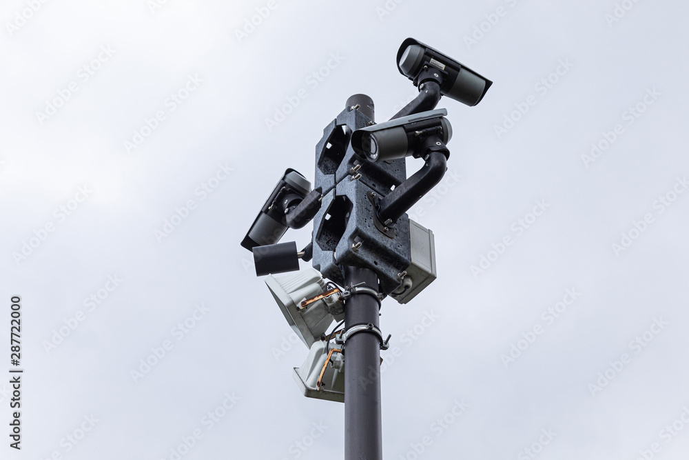 Black video monitoring cameras and street lamps on column against white sky Black video monitoring cameras and street lamps on column against white sky
