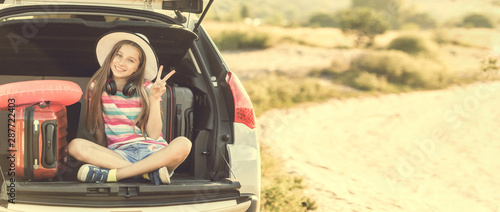 Little cute girl in the trunk of a car with suitcases