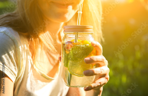 Girl drinking fresh lemonade in jars with straws. Hipster summer drinks. Eco-friendly in the nature. Lemons, oranges and berries with mint in the glass.