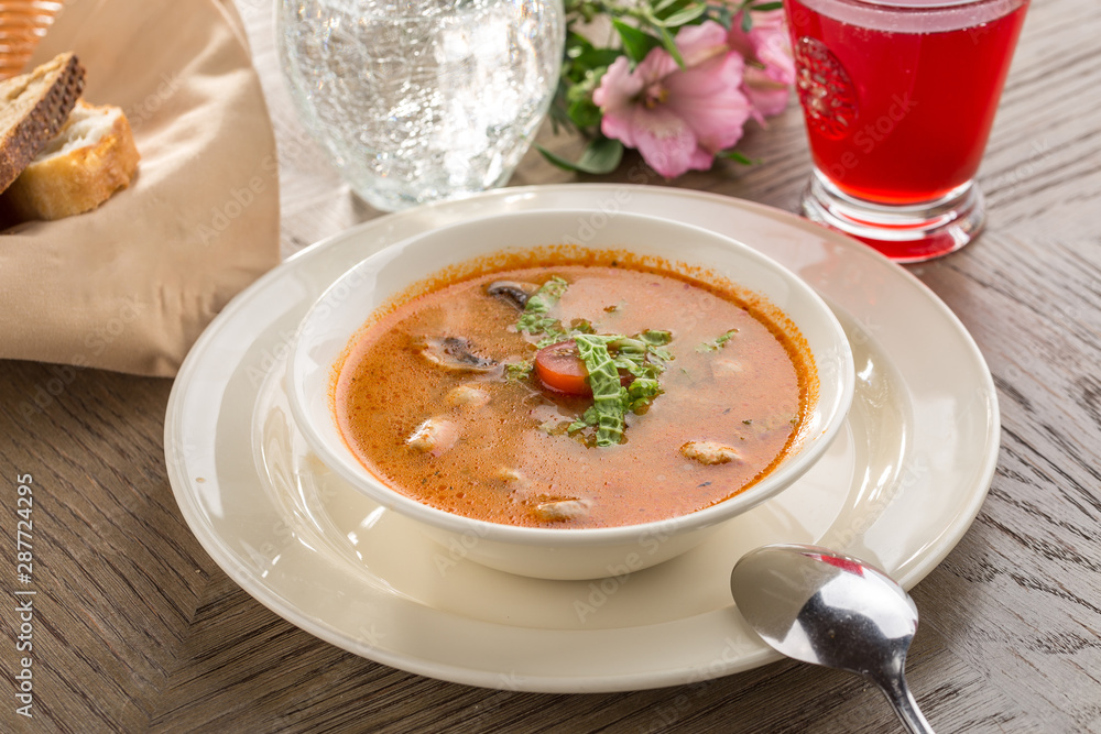 Hot and sour soup Tom Yum Goong with tomatoes and champignon and red drink on wooden table Hot and sour soup Tom Yum Goong with tomatoes and champignon and red drink on wooden table